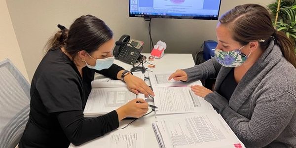 Two women wearing masks studying dental anatomy together at a desk.