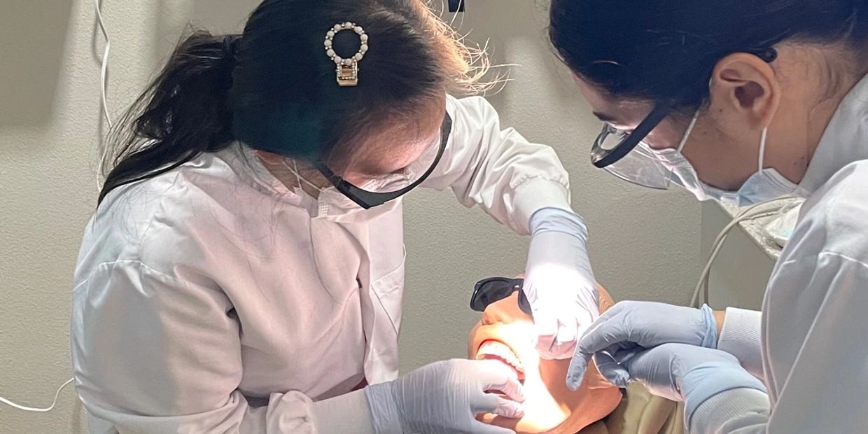 Two dental professionals examine a patient's teeth under bright light.