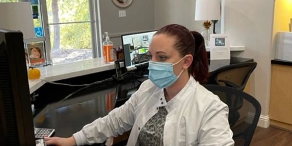 Healthcare worker wearing a mask at a reception desk using a computer.