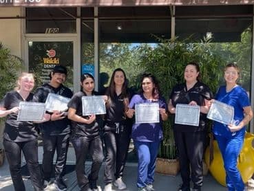 Roseville Dental Academy graduates holding certificates outside the academy.